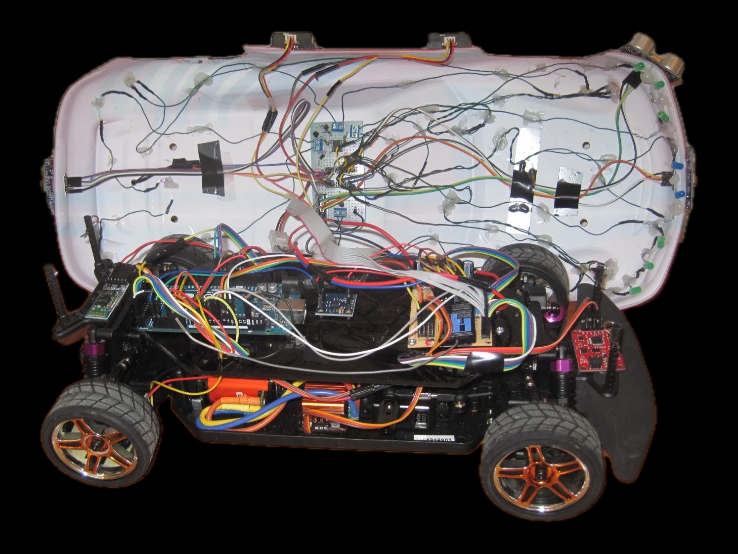 Autonomous RC car with its body shell lifted off, showing the Arduino, sensor boards and wiring on the chassis, and the ultrasonic sensors and indicator LEDs wired into the shell